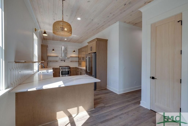 kitchen with wall chimney range hood, light brown cabinetry, premium appliances, light hardwood / wood-style floors, and kitchen peninsula