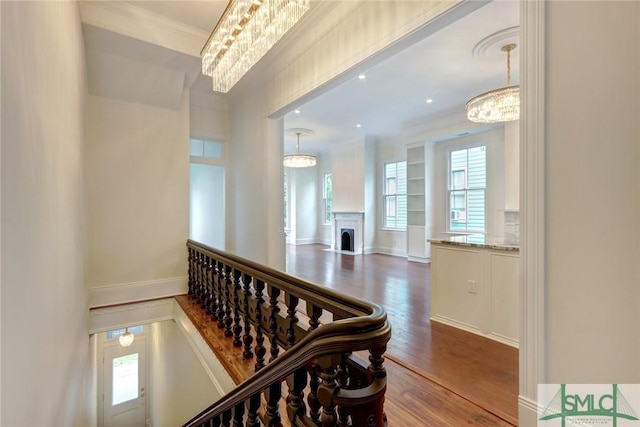 corridor with hardwood / wood-style floors, ornamental molding, and an inviting chandelier