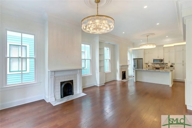 unfurnished living room with a tile fireplace, a chandelier, dark hardwood / wood-style floors, and ornamental molding