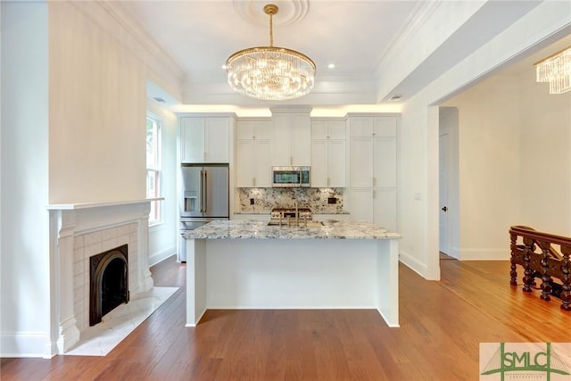 kitchen with light stone countertops, appliances with stainless steel finishes, hardwood / wood-style flooring, decorative light fixtures, and white cabinetry