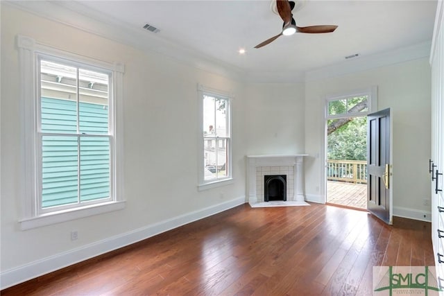 unfurnished living room featuring crown molding, dark wood-type flooring, a wealth of natural light, and a tiled fireplace