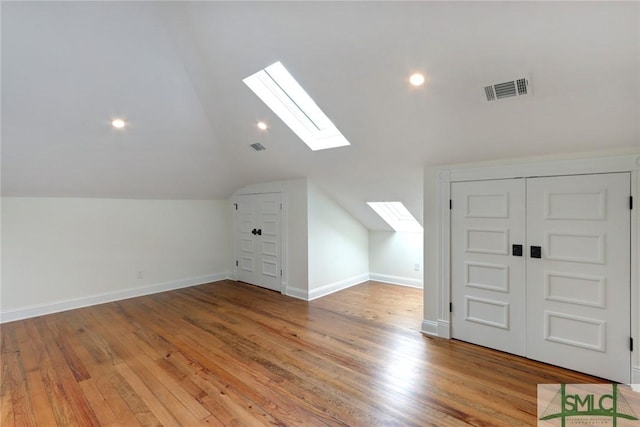 additional living space featuring vaulted ceiling with skylight and light hardwood / wood-style floors