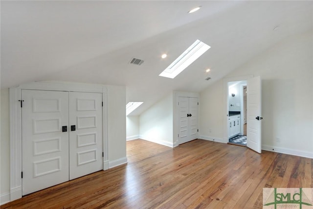 additional living space featuring vaulted ceiling with skylight and light hardwood / wood-style floors