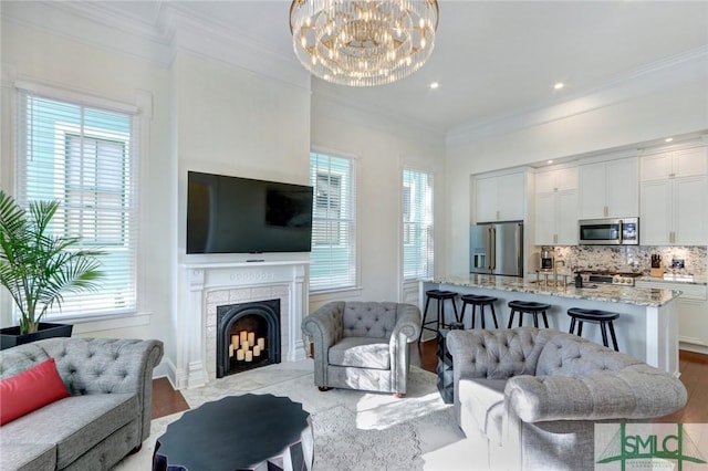 living room with light hardwood / wood-style floors, an inviting chandelier, ornamental molding, and a tiled fireplace