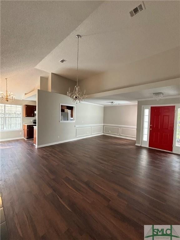 unfurnished living room with dark hardwood / wood-style floors, an inviting chandelier, and vaulted ceiling