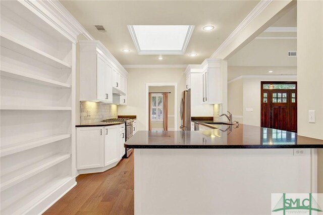 kitchen with kitchen peninsula, stainless steel appliances, white cabinetry, and a skylight