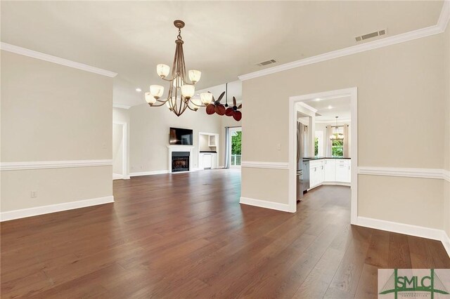 unfurnished living room featuring dark hardwood / wood-style flooring, an inviting chandelier, and ornamental molding