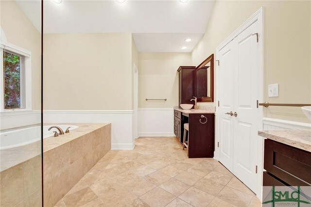 bathroom with tile patterned floors, vanity, and a relaxing tiled tub