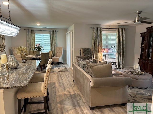 living room featuring ceiling fan with notable chandelier, light hardwood / wood-style floors, and a wealth of natural light