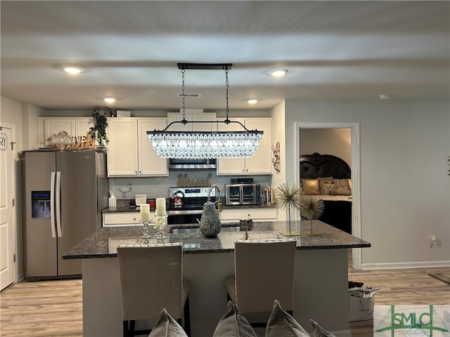 kitchen featuring stainless steel appliances, dark stone countertops, white cabinets, and a kitchen island with sink