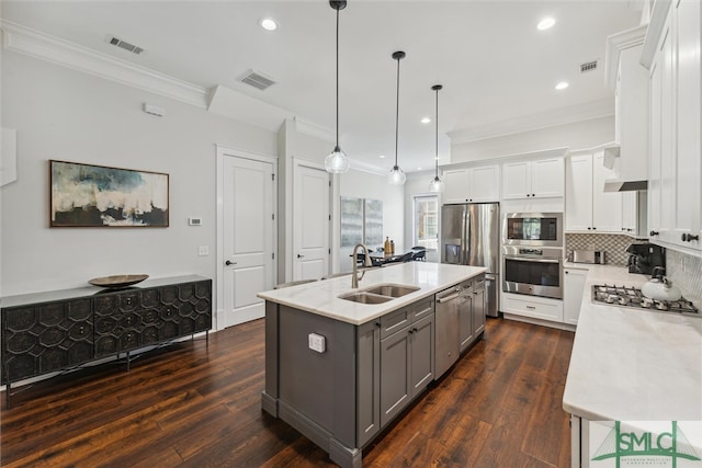 kitchen with white cabinets, dark hardwood / wood-style flooring, hanging light fixtures, appliances with stainless steel finishes, and a center island with sink