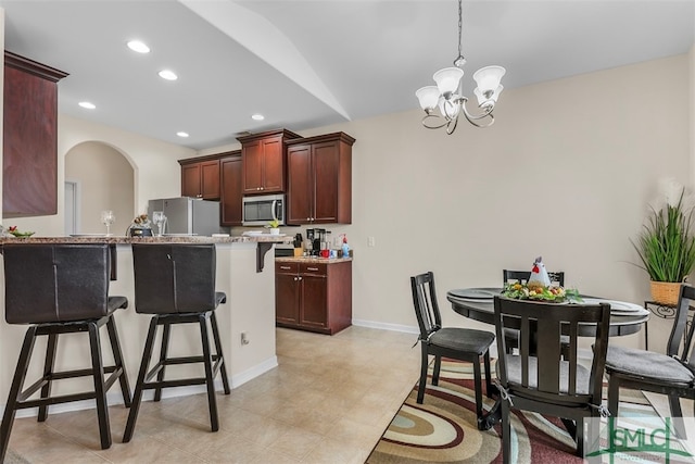 kitchen featuring pendant lighting, a notable chandelier, kitchen peninsula, appliances with stainless steel finishes, and a kitchen breakfast bar