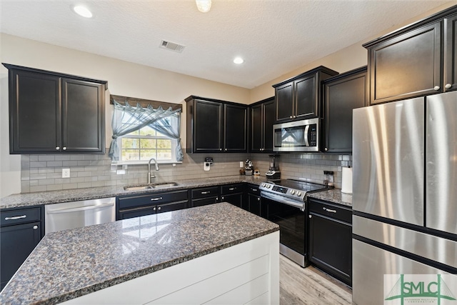 kitchen with appliances with stainless steel finishes, sink, dark stone counters, and a kitchen island