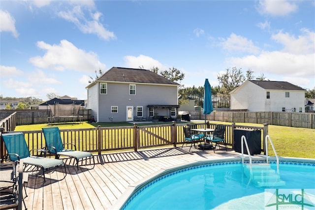 view of swimming pool with a trampoline, a yard, and a wooden deck