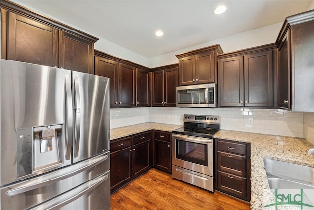 kitchen featuring decorative backsplash, dark brown cabinetry, light stone counters, stainless steel appliances, and dark hardwood / wood-style floors