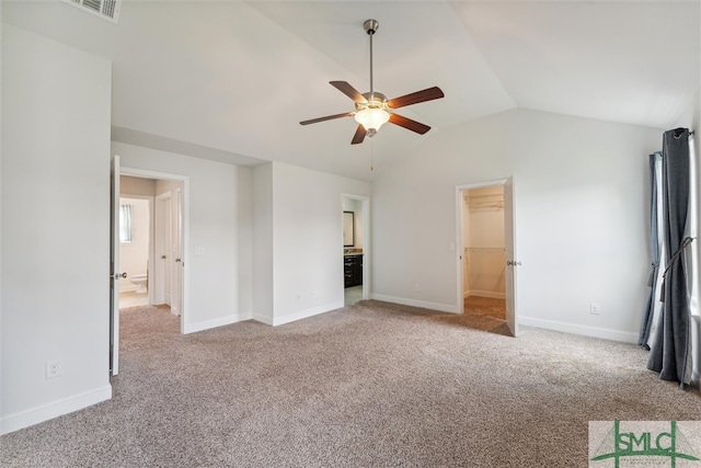 unfurnished bedroom featuring a spacious closet, vaulted ceiling, carpet, and ceiling fan