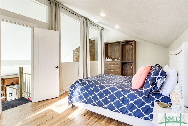 bedroom with vaulted ceiling, a textured ceiling, and light hardwood / wood-style floors