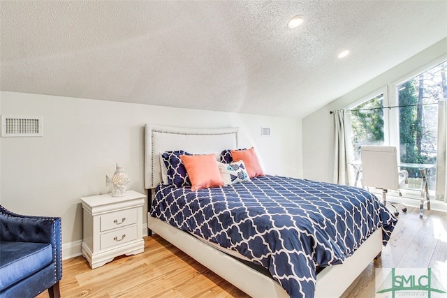 bedroom with vaulted ceiling, a textured ceiling, and light hardwood / wood-style floors