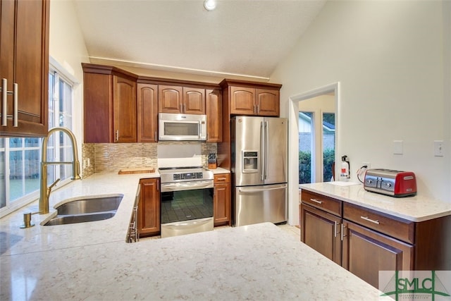 kitchen with light stone countertops, sink, vaulted ceiling, appliances with stainless steel finishes, and backsplash