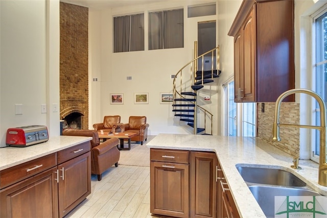 kitchen with tasteful backsplash, light hardwood / wood-style flooring, sink, light stone counters, and a fireplace