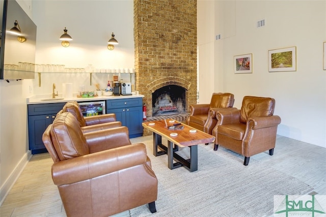 living room with a brick fireplace, wet bar, beverage cooler, light hardwood / wood-style floors, and a high ceiling