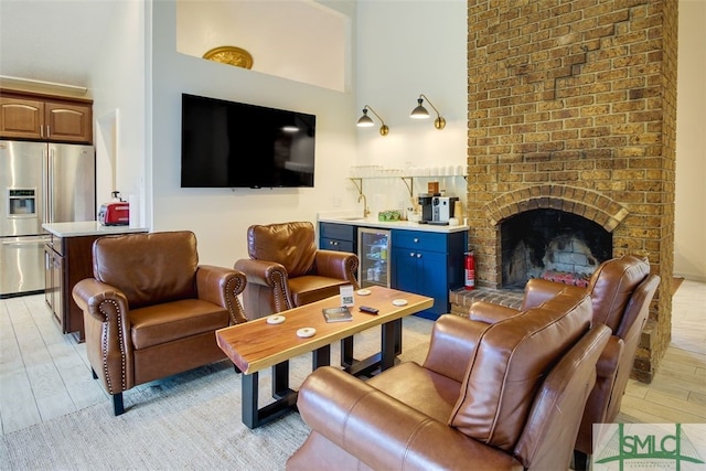 living room featuring a high ceiling, light wood-type flooring, a brick fireplace, and beverage cooler