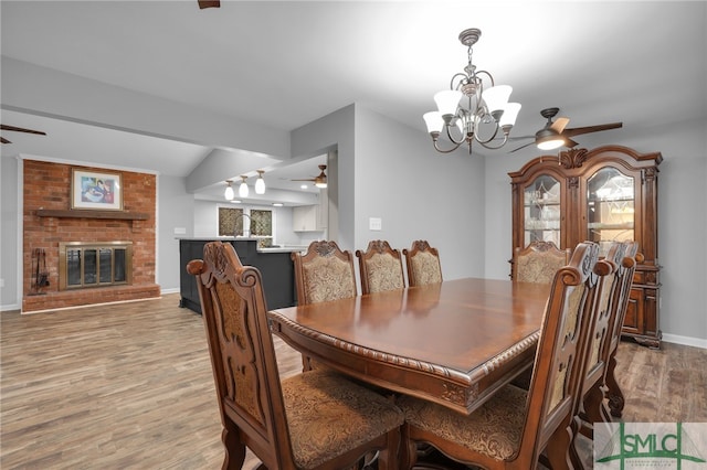 dining room with ceiling fan with notable chandelier, light wood-type flooring, a fireplace, and lofted ceiling