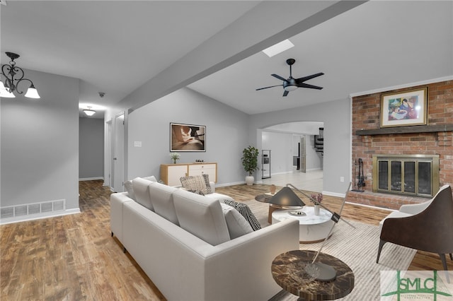 living room featuring a brick fireplace, vaulted ceiling with beams, light wood-type flooring, and ceiling fan with notable chandelier