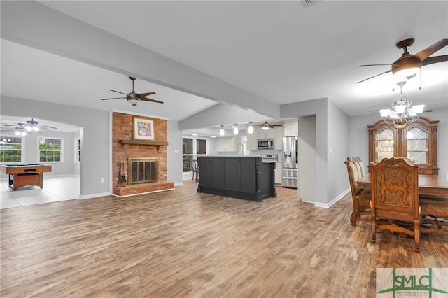 living room featuring a brick fireplace, light hardwood / wood-style flooring, lofted ceiling with beams, a notable chandelier, and billiards