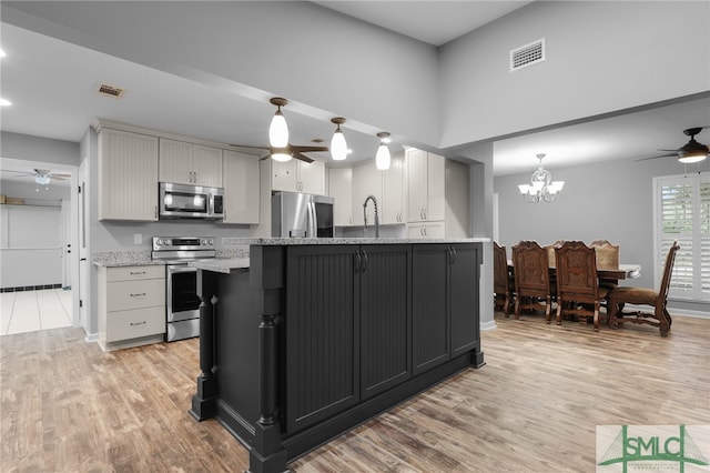 kitchen with light hardwood / wood-style floors, decorative light fixtures, appliances with stainless steel finishes, and an island with sink