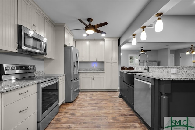 kitchen with light stone countertops, wood-type flooring, sink, white cabinetry, and appliances with stainless steel finishes