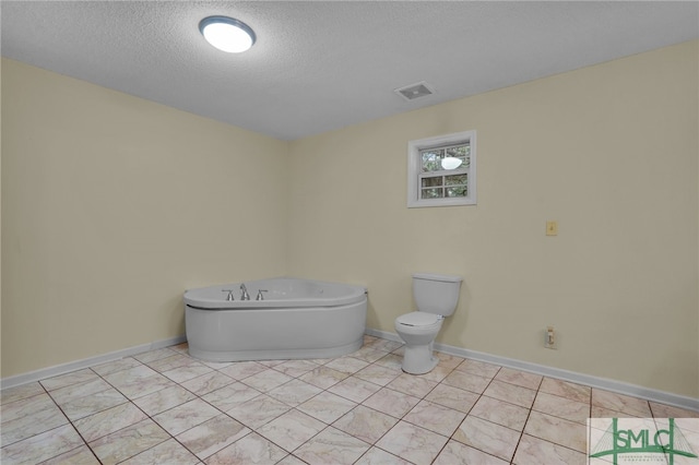 bathroom with a tub, toilet, and a textured ceiling