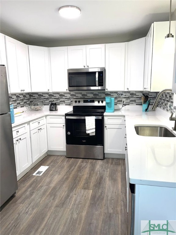 kitchen featuring white cabinets, hanging light fixtures, sink, stainless steel appliances, and dark hardwood / wood-style flooring