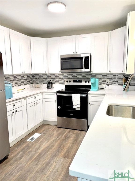 kitchen featuring stainless steel appliances, backsplash, hardwood / wood-style flooring, and white cabinetry