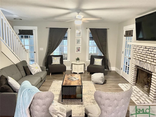 living room with ceiling fan, hardwood / wood-style flooring, and a brick fireplace