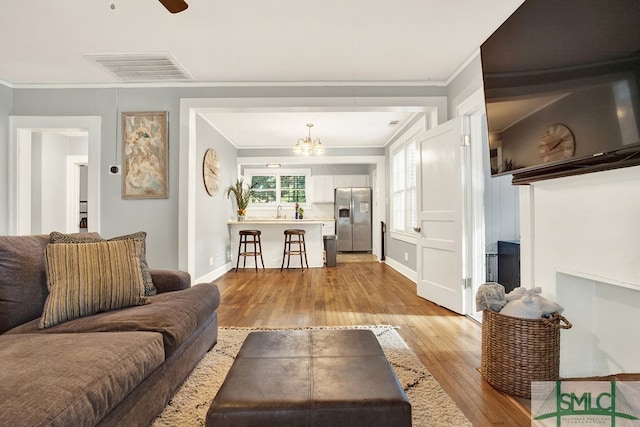 living room with ceiling fan with notable chandelier, light wood-type flooring, crown molding, and sink