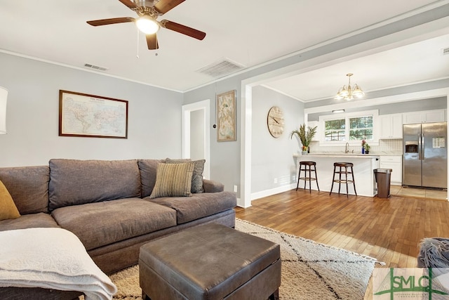 living room featuring ornamental molding, ceiling fan with notable chandelier, sink, and light hardwood / wood-style flooring