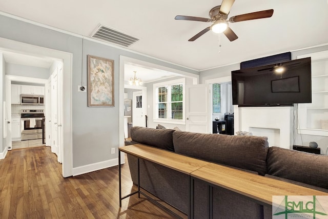 living room featuring ceiling fan with notable chandelier, ornamental molding, and dark hardwood / wood-style flooring