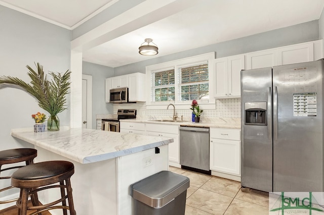 kitchen with appliances with stainless steel finishes, a kitchen bar, decorative backsplash, and white cabinetry