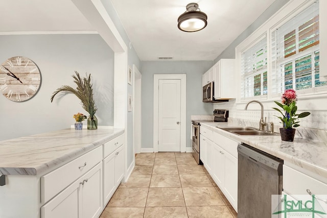 kitchen with light stone counters, white cabinets, sink, appliances with stainless steel finishes, and light tile patterned floors