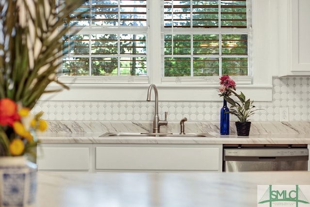 kitchen with light stone counters, stainless steel dishwasher, sink, white cabinetry, and backsplash