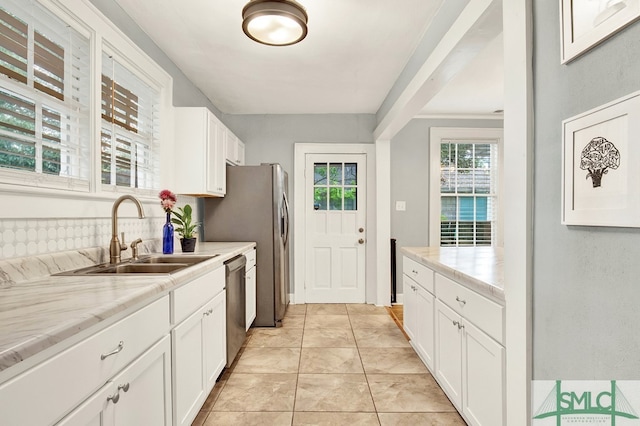 kitchen with light tile patterned floors, sink, white cabinetry, dishwasher, and light stone countertops