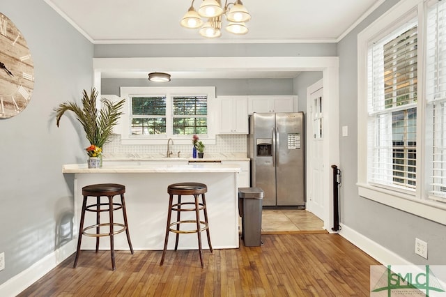 kitchen featuring backsplash, white cabinetry, stainless steel refrigerator with ice dispenser, a kitchen breakfast bar, and hardwood / wood-style flooring