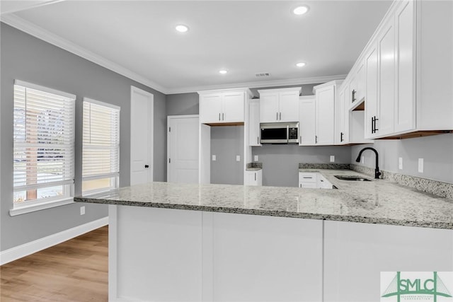 kitchen with white cabinets, kitchen peninsula, light stone countertops, and sink