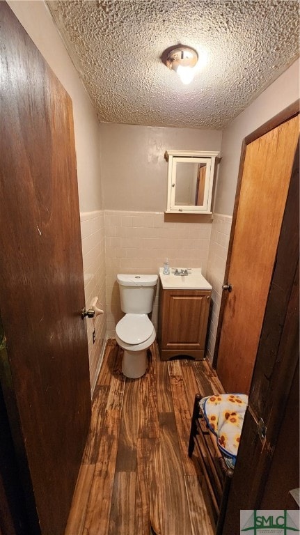 bathroom featuring vanity, wood-type flooring, tile walls, toilet, and a textured ceiling