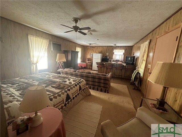 carpeted bedroom with white refrigerator, a textured ceiling, wooden walls, and ceiling fan