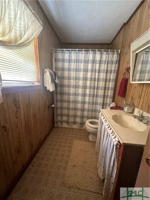 bathroom with curtained shower, wooden walls, vanity, and toilet