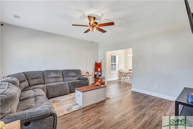 living room with dark wood-type flooring, a textured ceiling, and ceiling fan