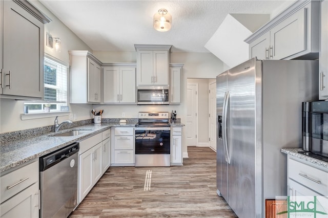 kitchen featuring light stone counters, light hardwood / wood-style flooring, a textured ceiling, sink, and appliances with stainless steel finishes