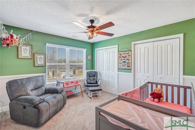 carpeted bedroom featuring multiple closets, a nursery area, a textured ceiling, and ceiling fan